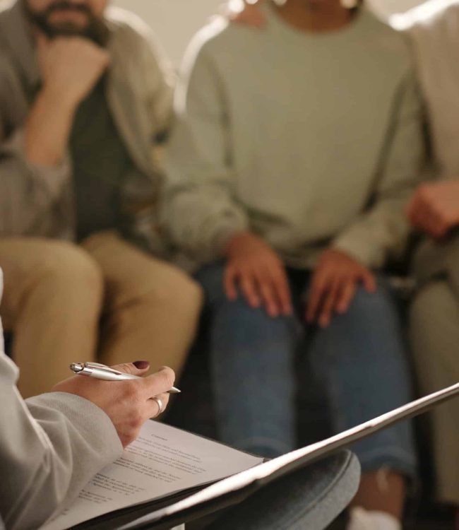 Close-up of social worker making notes in document while talking to foster parents at meeting at home